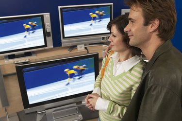 Couple standing by televisions in shop, smiling
