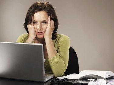 Woman sitting at laptop,  elbows on desk, holding head in hands