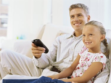 father sitting with his daughter holding a remote control