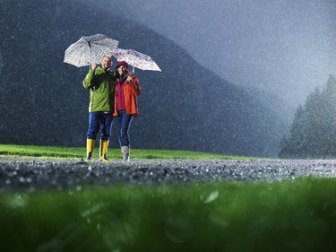 Man and woman with umbrellas playing in the rain.