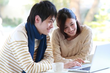 Man and woman sat smiling at laptop with cup and saucer