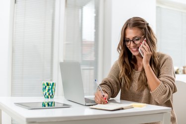 Young female writing notes while talking on phone