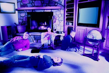 Wired family looking at viewer Father at laptop, mother holding phone, son in front of video game, daughter wearing headset