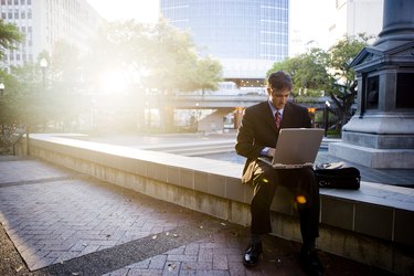 Businessman using laptop computer by sidewalk