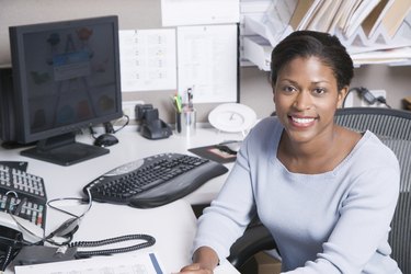 Woman sitting at desk in office, smiling, portrait