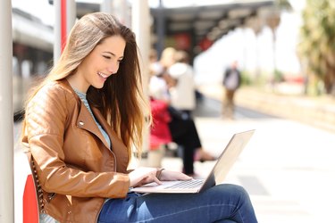 Girl using a laptop while waiting in a train station