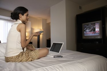 Businesswoman on hotel bed watching financial news