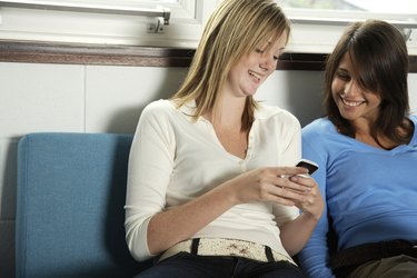 Two teenage girls (15-17) looking at mobile phone, smiling