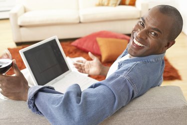 Mature man on sofa with laptop, smiling, portrait