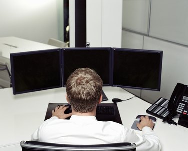Businessman at desk using computer with multiple screens, rear view