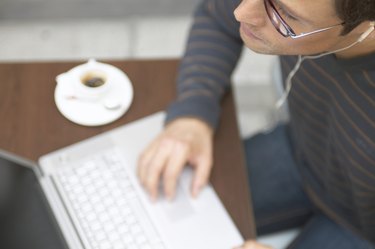 "Man sitting at cafe table using laptop computer, close-up"