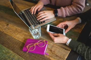 Hands over laptop and smartphone on wooden table with glasses