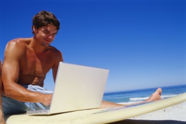 Low angle view of a young man using a laptop on a surfboard