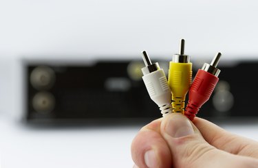 AV cable connectors in hand with AV receiver on background