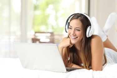 Girl with headphones reading in a laptop at home