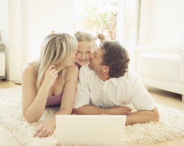 Mother and father kissing girl on rug