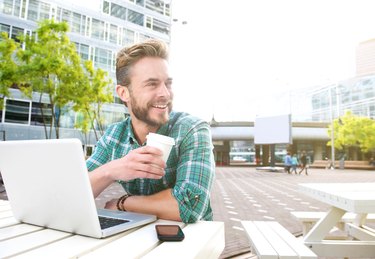 Smiling man sitting outside with laptop and coffee