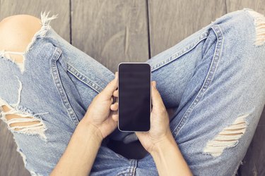 Girl in jeans with smartphone on the wooden floor