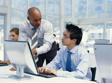 Businessman pointing at computer monitor and explaining to man