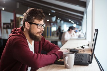 Young man in glasses sitting and using laptop