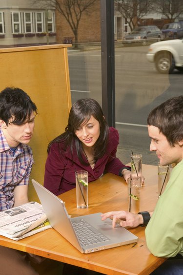 Caucasian Twenty Somethings Sitting In An Internet Cafe And Laughing While Looking At A Laptop Computer