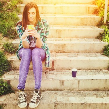 Teenage girl with smartphone and takeaway coffee texting