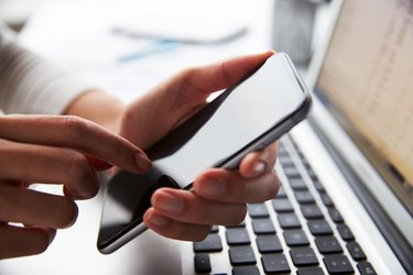 Close-up of a person using a smartphone at their laptop