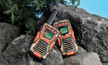 Photo of a pair of Cobra CXT 1035 FLT CAMO  two-way radios in a rocky setting.