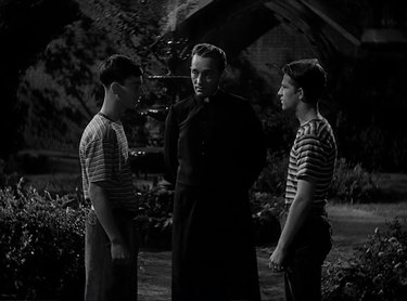 Still of Father O'Malley standing between two boys.