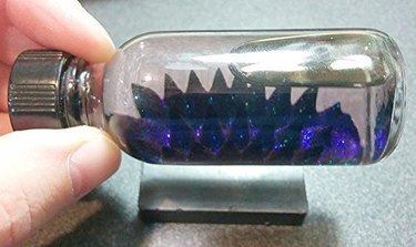 Photo of sparkling blue ferrofluid in a bottle reacting to a magniet.