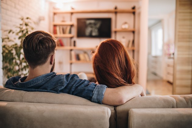 Rear view of loving couple watching TV at home.