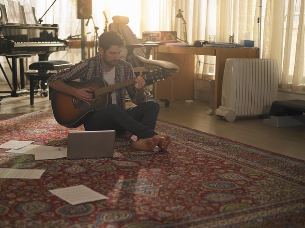 A man playing guitar next to a laptop