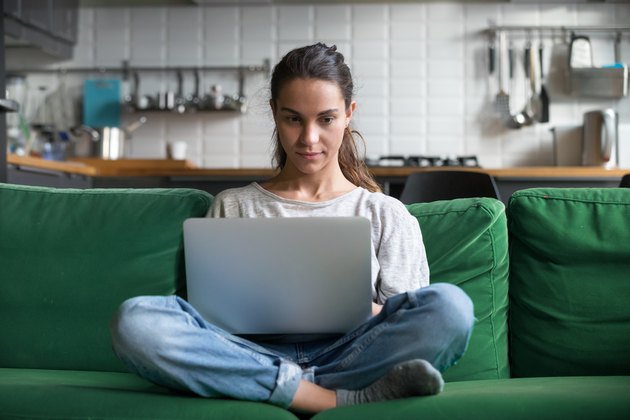 Serious woman using laptop checking news online sitting on sofa