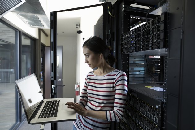 Female Filipino IT technician working at laptop in server room