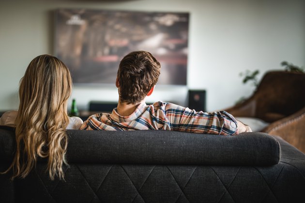 Back view of a couple watching TV on sofa at home.