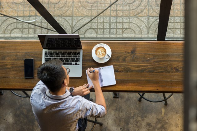 Young Asian businessman taking note beside laptop on wooden table