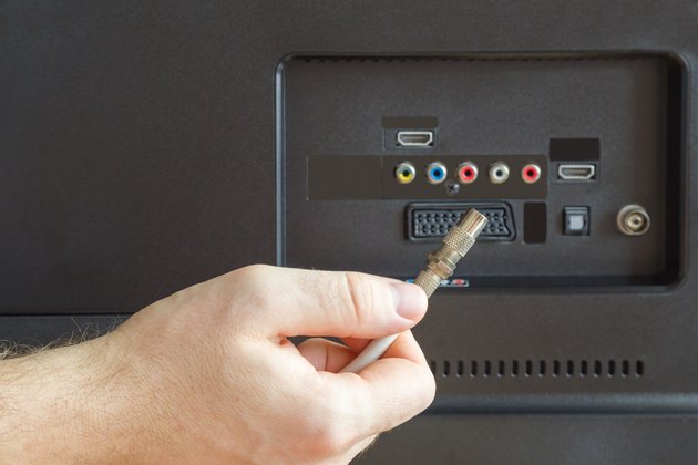 Man's hand holding coaxial cable. Back of tv. Television signal. Problem and solution.
