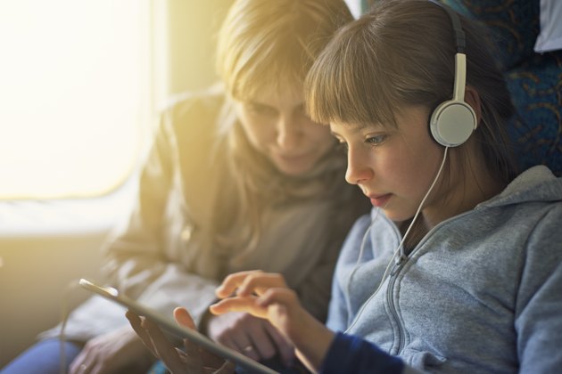 Girl with mother travelling on train and playing on tablet