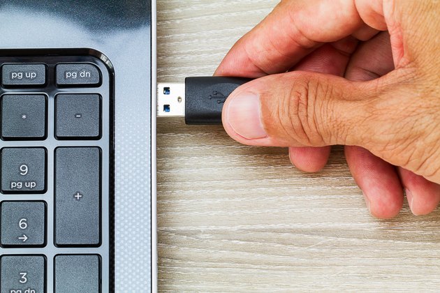 Hand connecting USB cable to laptop computer on wooden desk