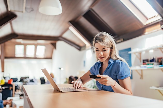 Lovely blonde woman holding credit card and using laptop.