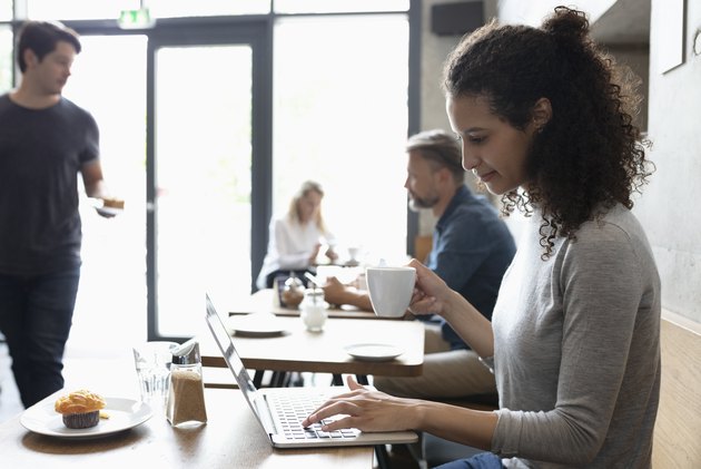 Woman using laptop, drinking coffee in cafe