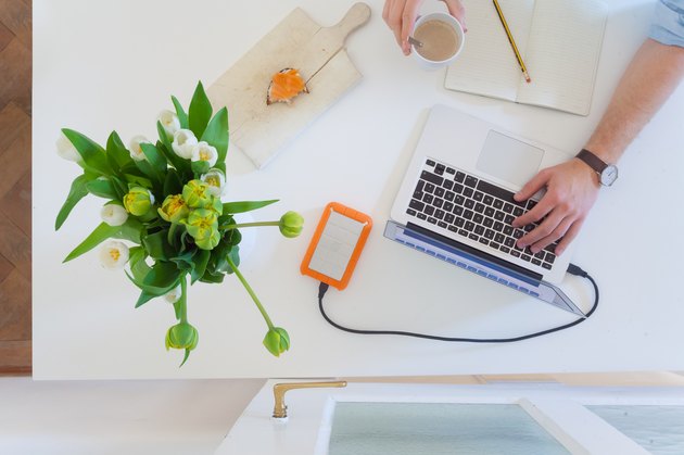 Man working at home office with laptop while drinking coffee