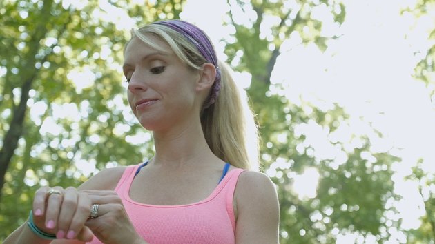 Blonde athletic woman checking fitbit device after running off road