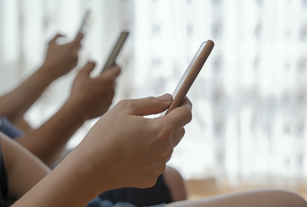 Shot of a group of unrecognizable people using their mobile phones together at home