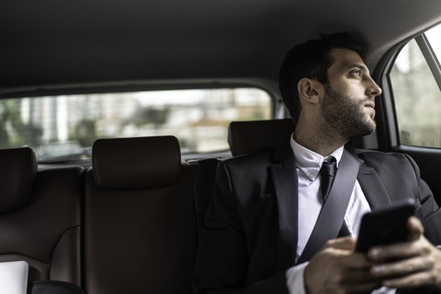 Businessman using cellphone in a cab and looking through window