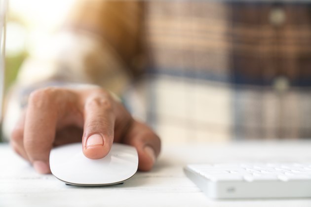 Male hand holding computer mouse with laptop keyboard in the background