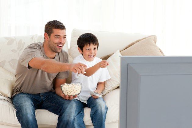 Happy father and son watching television while eating pop corn