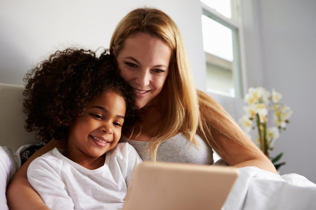 Caucasian mum and black daughter use tablet in bed, close-up
