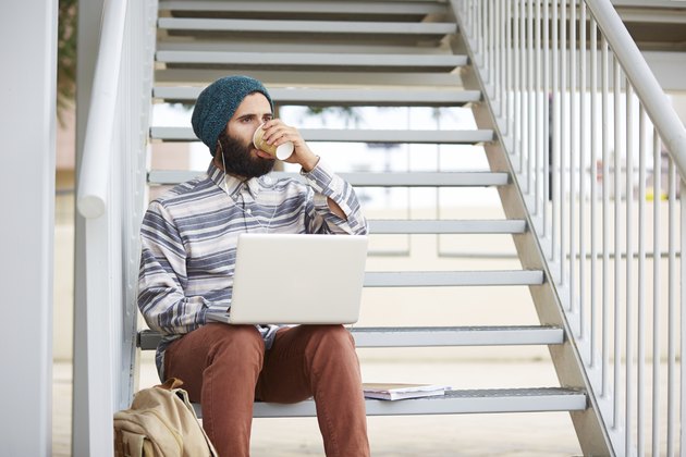 Young bearded hipster student using computer outdoors