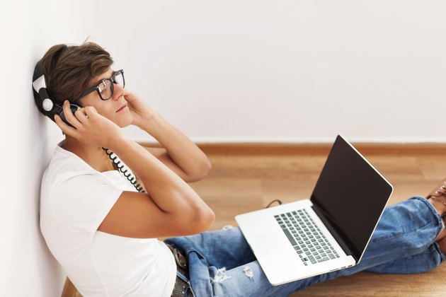 Handsome hipster sitting up against wall listening to music